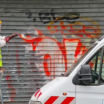 Man cleaning graffiti of a sprayed metal door